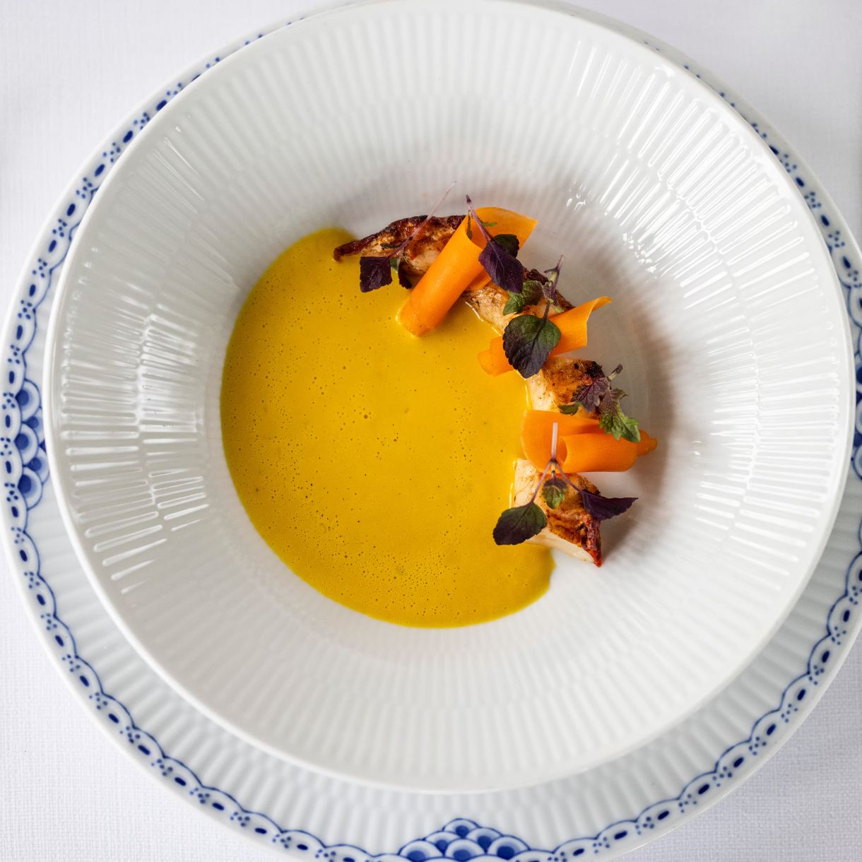 Anretning med fisk, gulerodsbånd, pyntegrøn med en gul sauce.