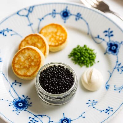 Kaviarservering med blinis, creme fraiche og purløg på porcelænstallerken.
