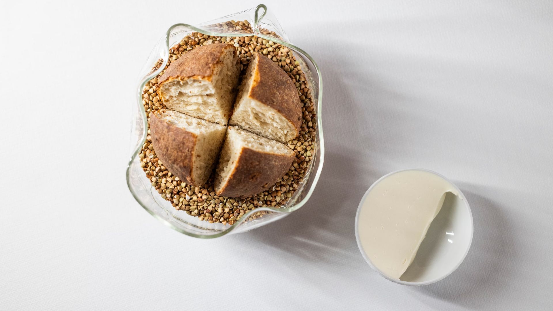 Rundt brød i glasfad med boghvede og cremet smørservering.