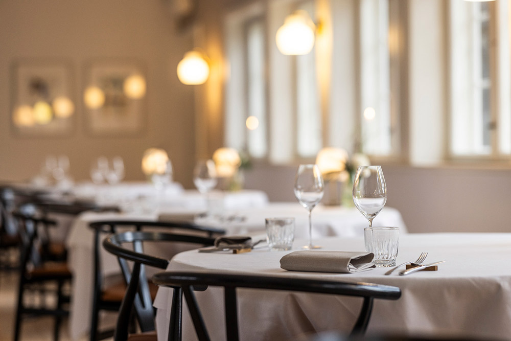 Lyst restaurantlokale med runde borde dækket op til service.